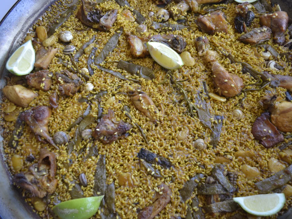 Valencian paella with chicken, rabbit, flat beans, and snails in a wide pan