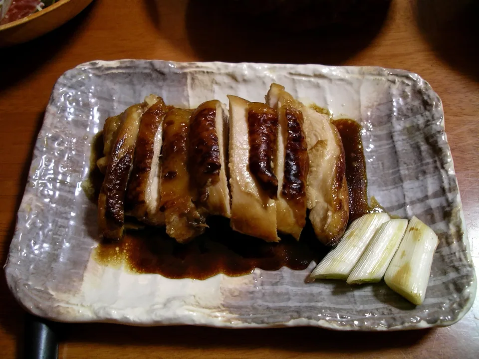 ไก่เทอริยากิหั่นชิ้นเคลือบซอสเงาและหนังเกรียม เสิร์ฟกับต้นหอมญี่ปุ่นย่าง