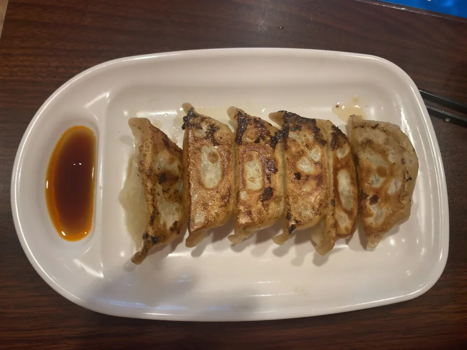 Six pan-fried Japanese gyoza in a row with crisp browned bottoms and a dark soy-vinegar dip in a white rectangular plate