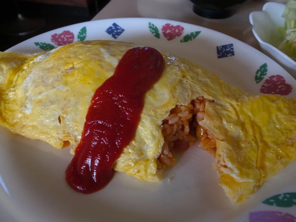 Fully set thin omelette cut open to show chicken ketchup rice with one broad ketchup stripe and no garnish
