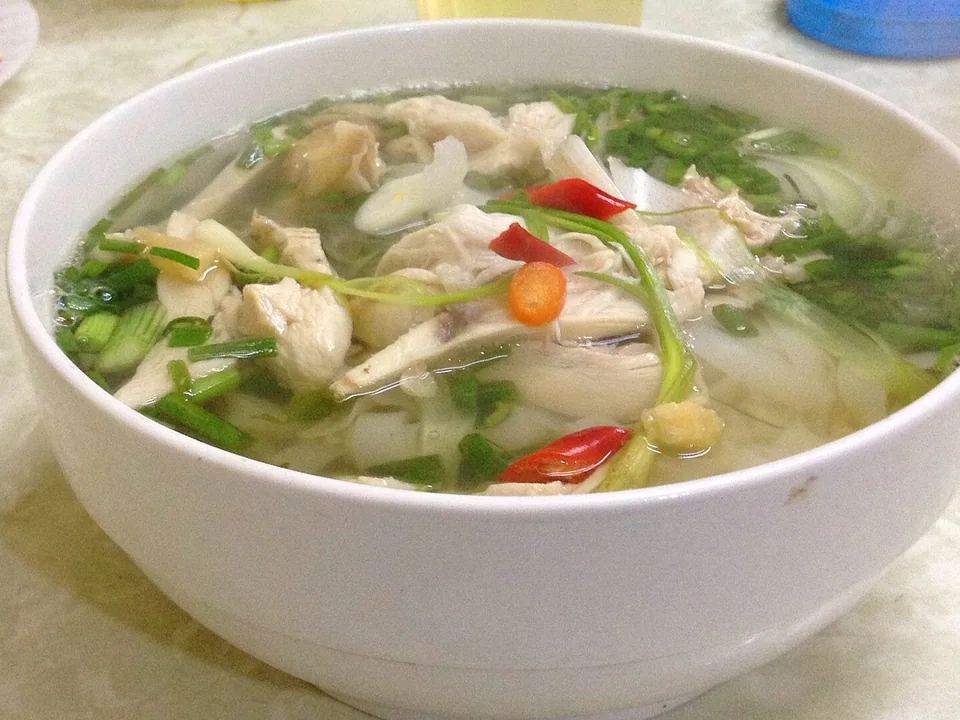 เฝอไก่กับไก่หั่นและสมุนไพรในน้ำซุปใสสีทอง