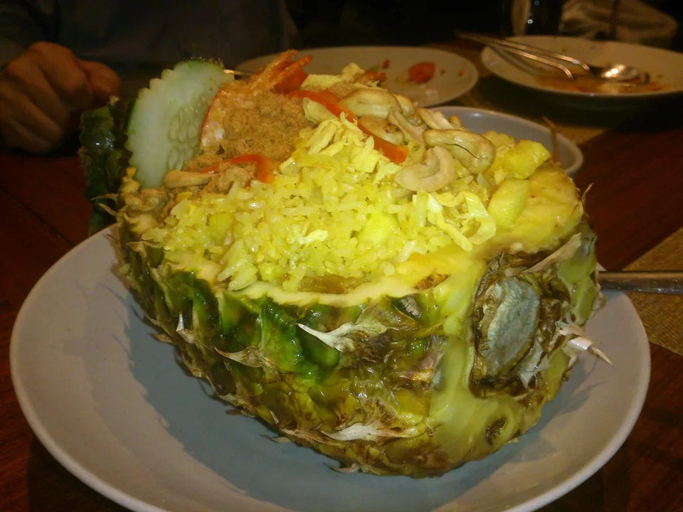 ข้าวผัดสับปะรดในเปลือกกับกุ้ง ไข่ ผงกะหรี่ เม็ดมะม่วง ลูกเกด ต้นหอม และมะนาว