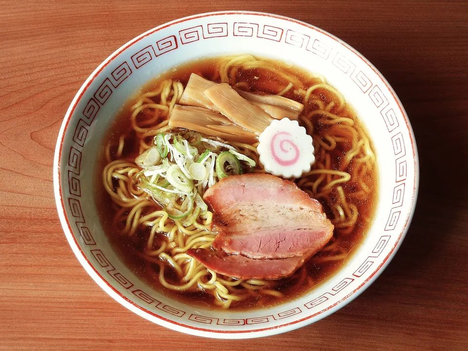 澄んだ濃いしょうゆスープに黄色い縮れ麺、厚いチャーシュー2枚、メンマ、なると、刻みねぎが見える実写写真。卵とのりはない。